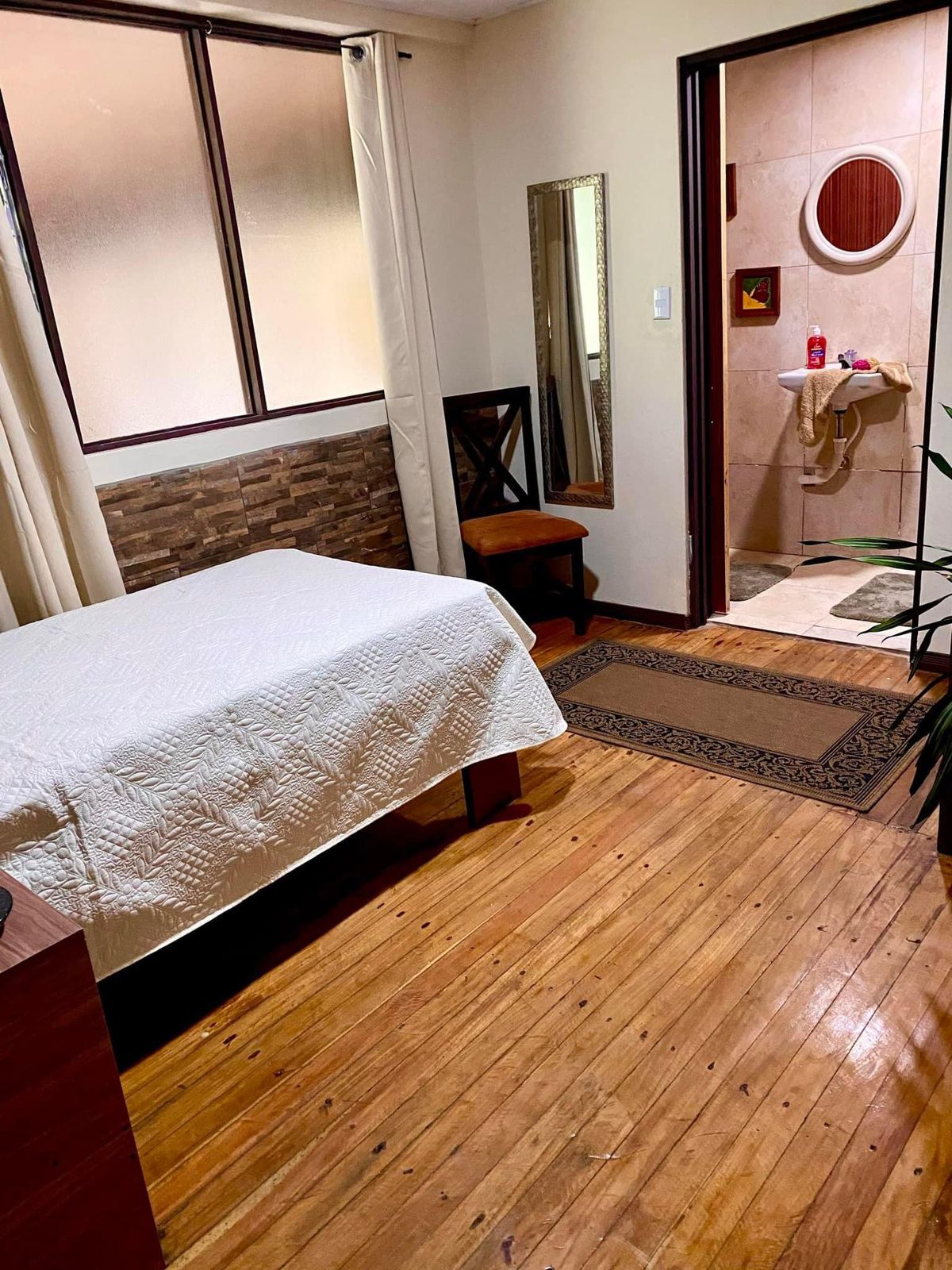 Cuarto con piso de madera, cama matrimonial y baño privado al fondo