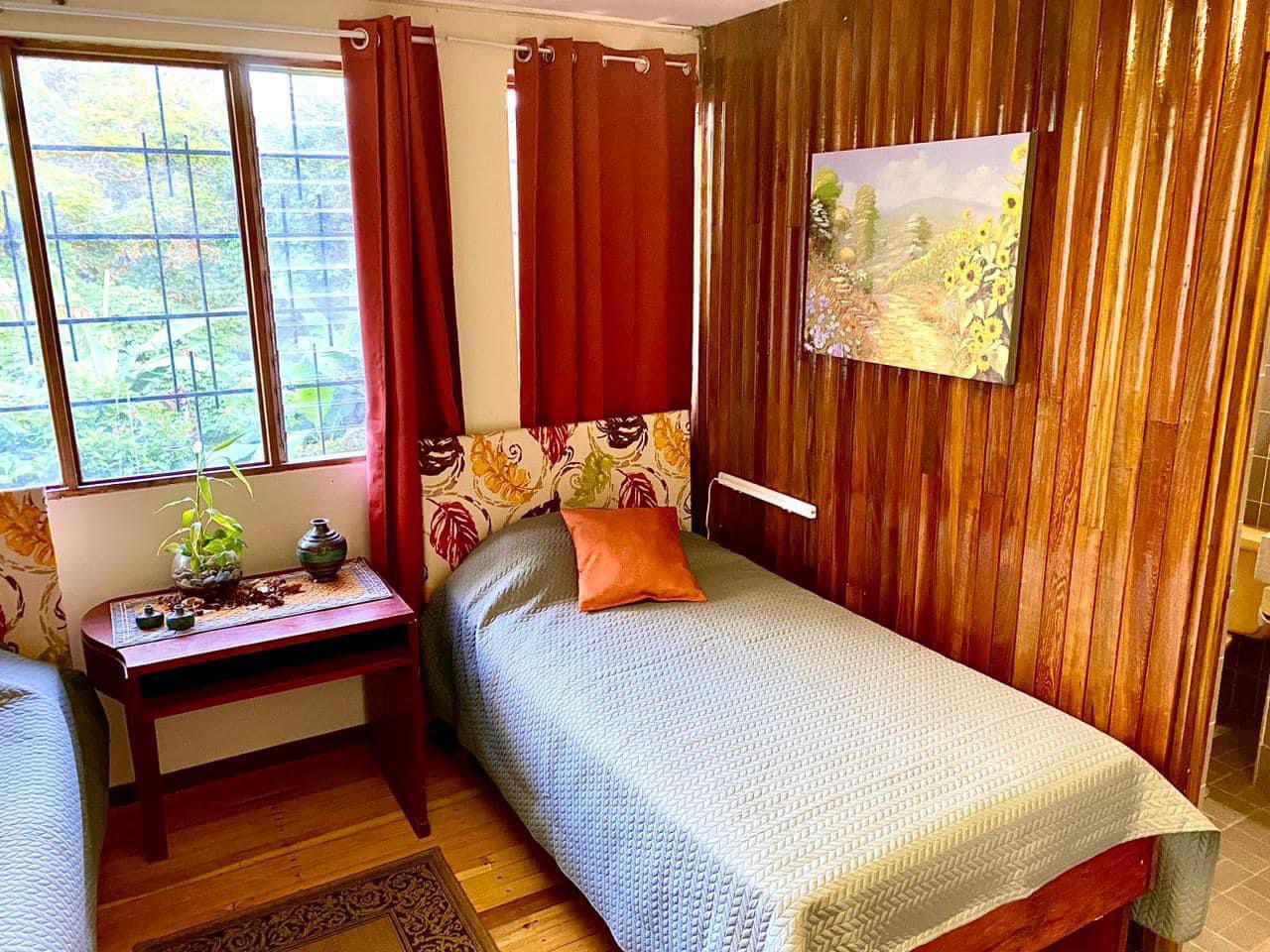 Cuarto con paredes de madera, dos camas y ventana con vista al jardín